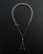 A silver-coloured stainless steel chain necklace featuring a wide, interlocking circular link pattern that transitions into a thinner, adjustable box chain. The necklace includes a small, circular charm with a smiley face icon near the clasp area.