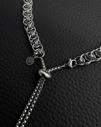 A silver-coloured stainless steel chain necklace featuring a complex interlocking circular link pattern. The necklace includes a sliding adjustable bead mechanism with two thin box chains hanging down and a small circular charm with a smiley face icon.