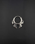 Handmade stainless steel tribal hoop earring with a spiky symmetrical design on a dark background designed as alternative rave jewelry. A silver-toned circular septum ring featuring a decorative, symmetrical tribal-inspired design with pointed, flame-like protrusions extending from the bottom half of the hoop. The metal has a polished, reflective finish. cyber sigilism style
