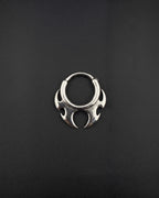 Handmade stainless steel tribal hoop earring with a spiky symmetrical design on a dark background designed as alternative rave jewelry. A silver-toned circular septum ring featuring a decorative, symmetrical tribal-inspired design with pointed, flame-like protrusions extending from the bottom half of the hoop. The metal has a polished, reflective finish. cyber sigilism style