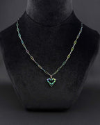 An iridescent oil-slick coloured, rainbow, stainless steel necklace featuring a paperclip style chain and a central heart-shaped pendant. The metal finish displays shifting hues of blue, green, and purple across the entire surface of the chain and the heart charm.