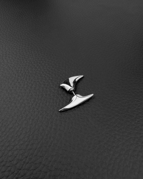 A silver-toned stainless steel ear cuff featuring two distinct, smooth, pointed, and curved metal spikes. The larger, elongated spike rests along the upper outer edge of the ear, while the smaller, tapered spike sits below the earlobe, creating a sleek look.