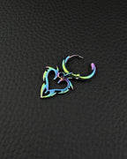 An iridescent rainbow-coloured stainless steel hoop earring featuring a dangling cybersigilism flaming heart shaped charm with sharp, flame-like edges. The metal displays a gradient of blue, green, and purple hues, creating a metallic, multi-coloured finish on the hoop and pendant.
