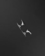 A silver-toned stainless steel ear cuff featuring two distinct, smooth, pointed, and curved metal spikes. The larger, elongated spike rests along the upper outer edge of the ear, while the smaller, tapered spike sits below the earlobe, creating a sleek look.