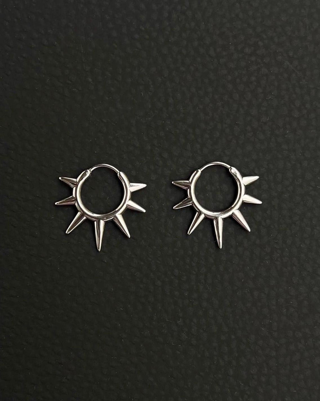 A pair of silver hoop earrings with a sunburst design. Each earring has a circular hoop with multiple pointed spikes radiating outwards. Handmade stainless steel earrings with a geometric sun design.