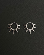 A pair of silver hoop earrings with a sunburst design. Each earring has a circular hoop with multiple pointed spikes radiating outwards. Handmade stainless steel earrings with a geometric sun design.