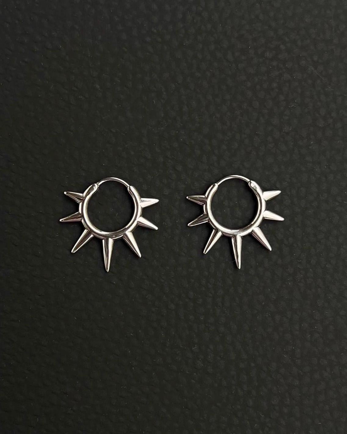 A pair of silver hoop earrings with a sunburst design. Each earring has a circular hoop with multiple pointed spikes radiating outwards. Handmade stainless steel earrings with a geometric sun design.